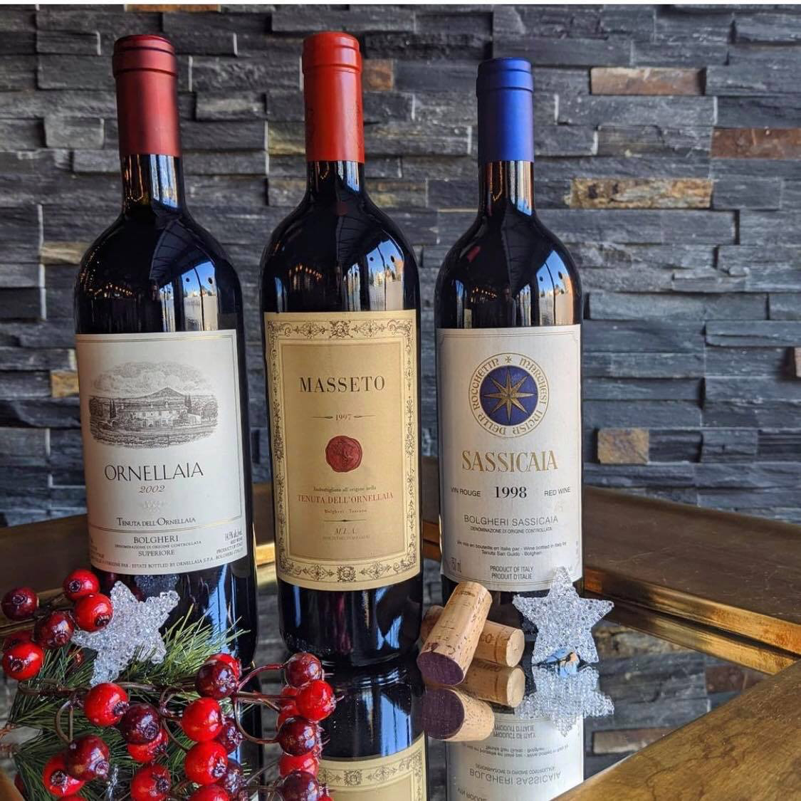 Three bottles of wine sitting on a table with a sprig of holly berries.