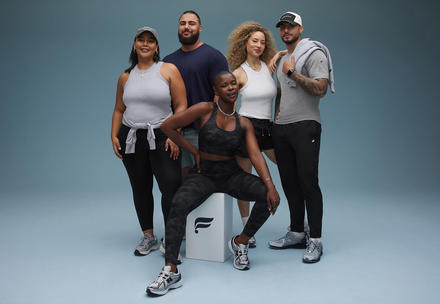Fabletics campaign photo featuring five male and female models wearing grey, black, and navy looks